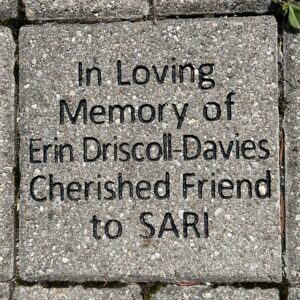 A grey brick laid into the ground that reads "In memory of Erin Driscoll-Davies cherished friend to SARI"