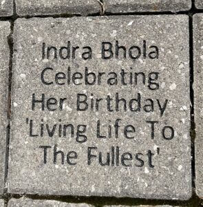 A grey brick laid into the ground that reads "Indra Bhola celebrating her birthday 'living life to the fullest'"
