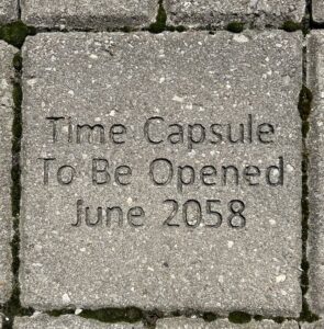 A grey brick laid into the ground that reads "Time capsule to be opened June 2058"