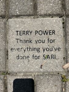 A grey brick laid into the ground that reads "TERRY POWER thank you for everything you've done at SARI"